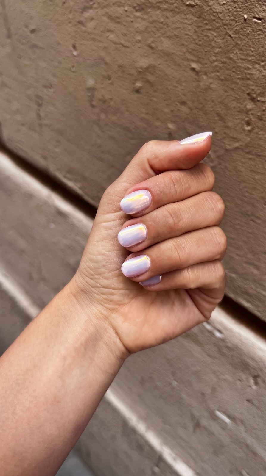 Manicura lila con efecto perla sobre una pared de estuco