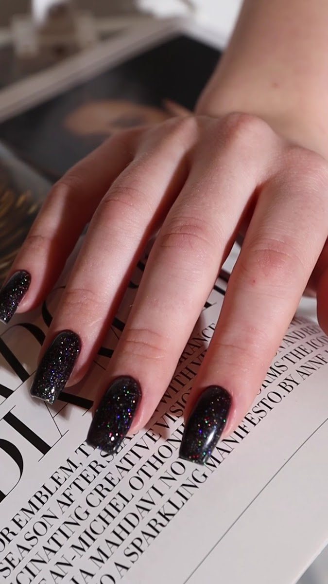 Uñas largas en negro con purpurina sobre las páginas de una revista