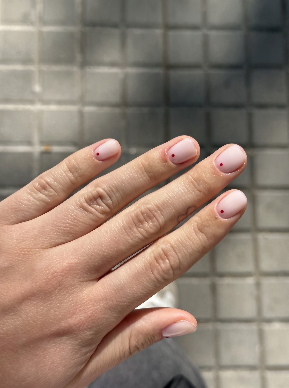 Manicura rosa pálido con un pequeño punto granate en cada uña, sobre baldosas de Barcelona