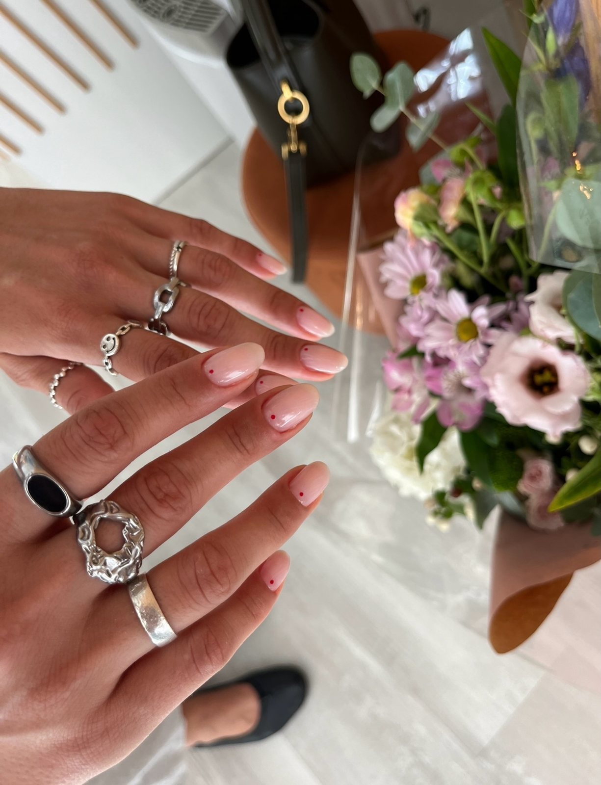 Manos con anillos de plata y manicura nude junto a un ramo de flores