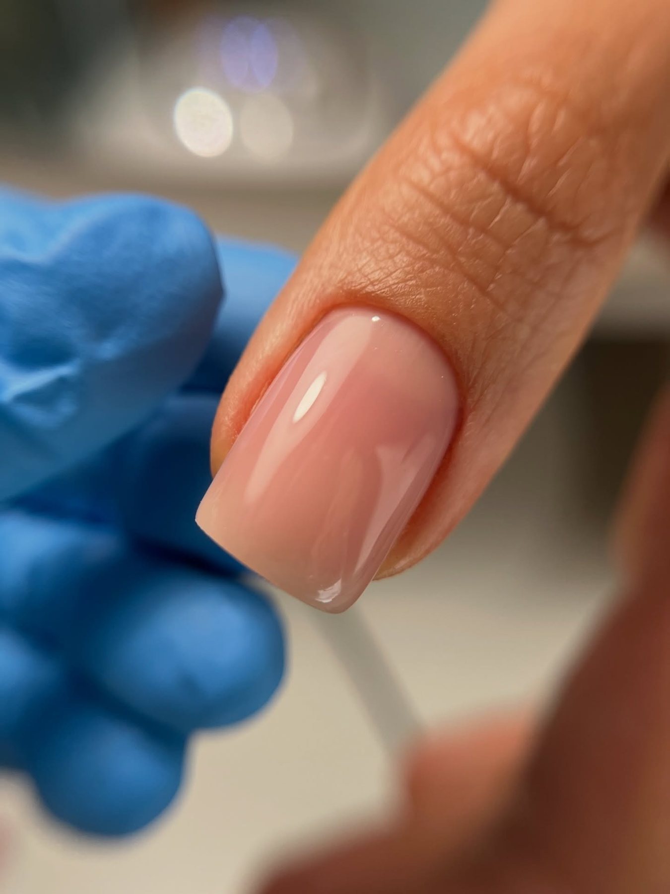 Uña natural recién esculpida en tono nude, sujetada por una mano con guante azul